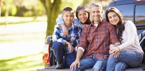 family sitting together in back of truck camping