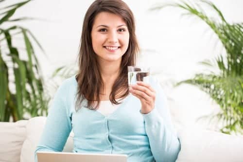 woman sitting on couch holding glass of water and laptop computer