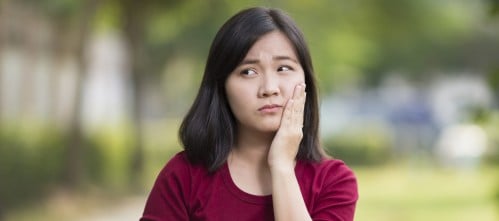 woman holding her cheek looking worried outside